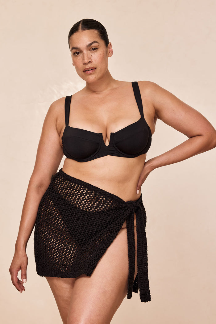 Three-quarter view of Santa Marta Sarong in black petit crochet showcasing sheer open-knit fabric and adjustable wrap-tie on neutral backdrop