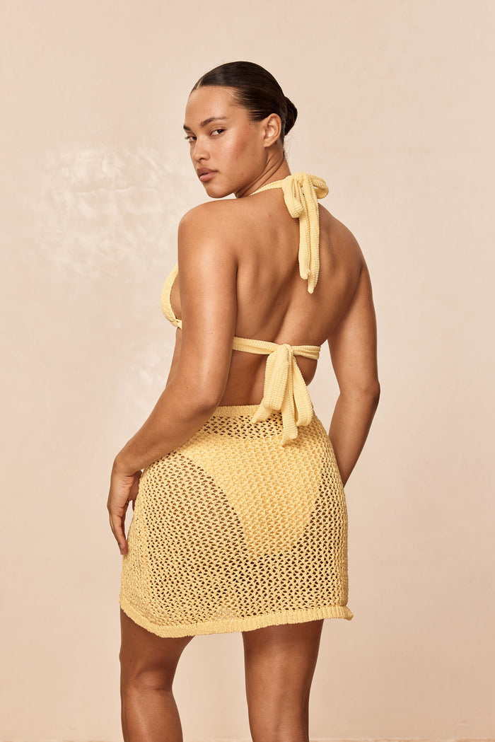 Back view of Santa Marta Sarong in Honey Petit Crochet showing open-knit crochet and mid-thigh length on beige background
