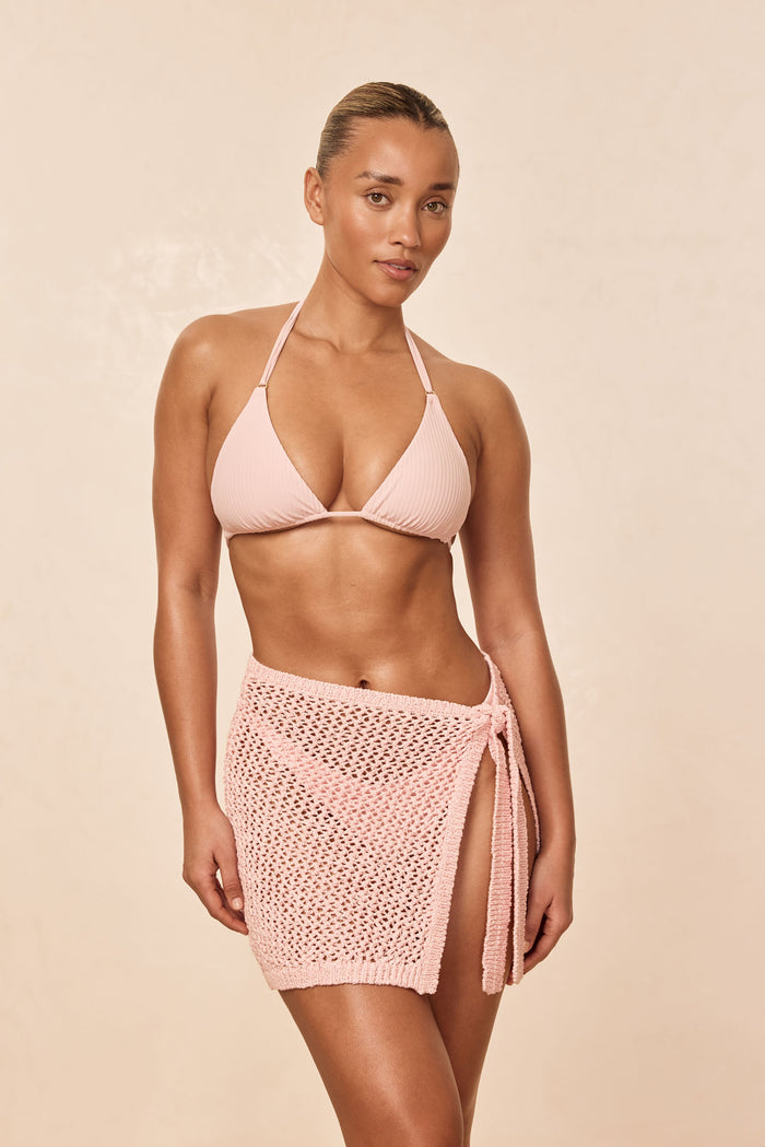 Front view of Santa Marta sarong in powder pink petit crochet, tied at hip with side slit, on model against beige background