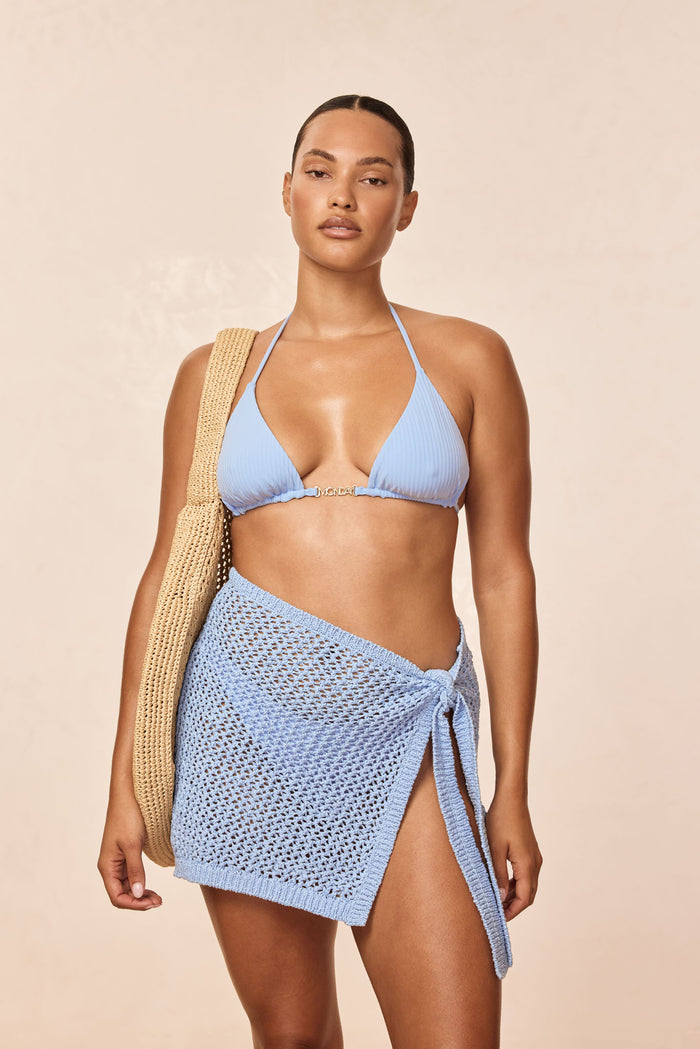 Front view of Santa Marta sarong in Sky Petit Crochet showing open knit fabric and side tie on model against beige background