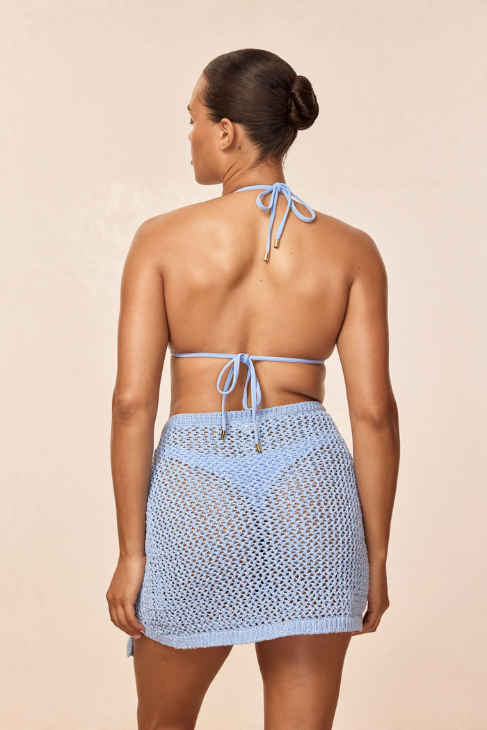 Back view of Santa Marta Sarong in Sky Petit Crochet showcasing sheer crochet knit wrap tied at waist on beige background