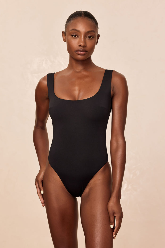 Front view of Sardinia One Piece in black showcasing square neckline, high leg and moderate coverage on model, beige backdrop
