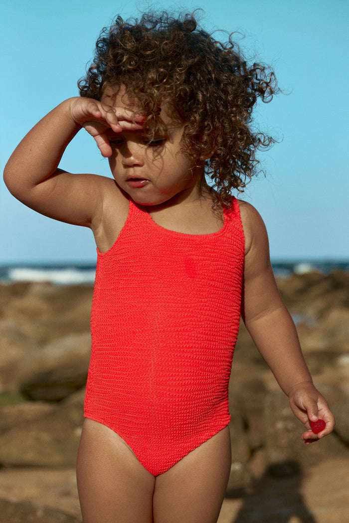 Front view of Sardinia One Piece in chili pepper crinkle showcasing textured fabric and scoop neck on a toddler at the beach