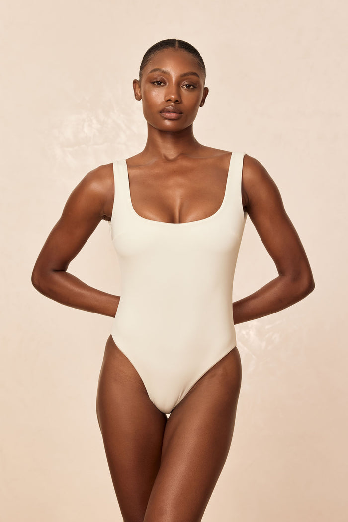 Front view of Sardinia one-piece swimsuit in ivory showcasing square neckline and high-cut leg against a light beige studio background