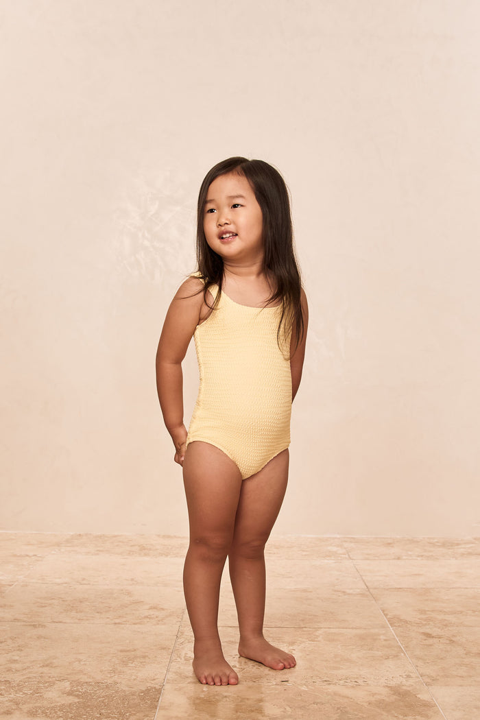 Front view of Sardinia kids one-piece swimsuit in honey crinkle on child model showing crinkle texture and scoop neckline