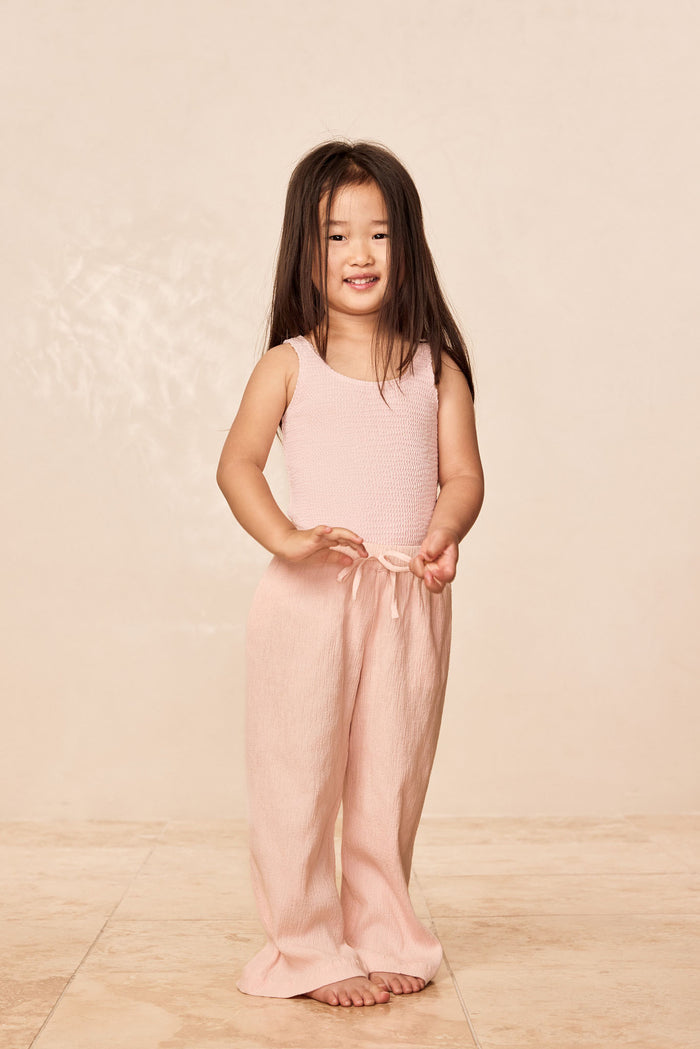 Front view of Sardinia kids one piece in Powder Pink Crinkle showing scoop neckline and textured fabric on pale beige background