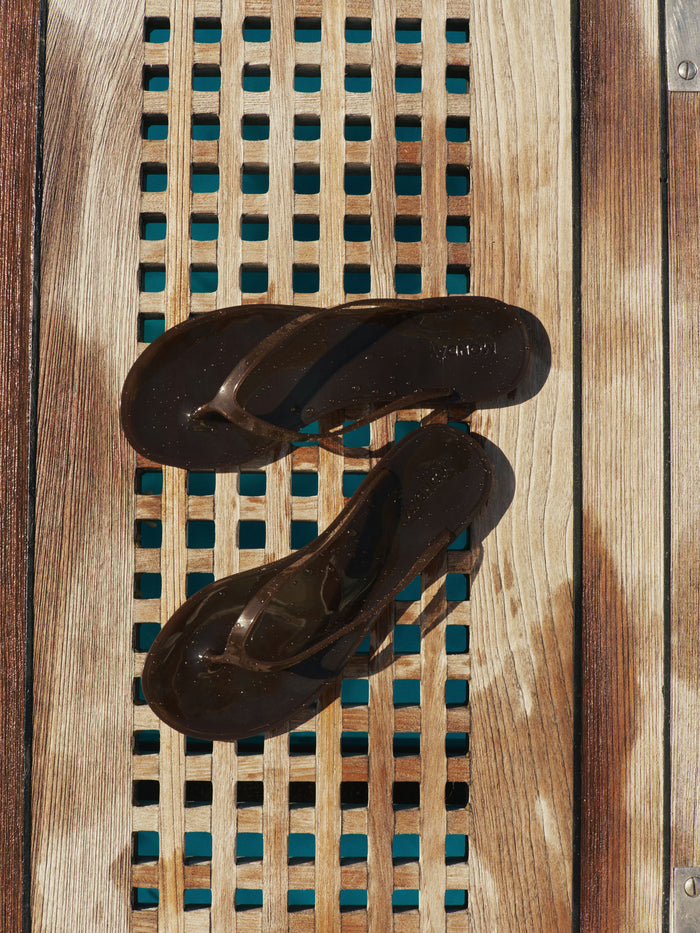 Top-down view of Sardinia Sandal in Espresso with glossy jelly straps and debossed MONDAY heel logo on a wooden slatted deck