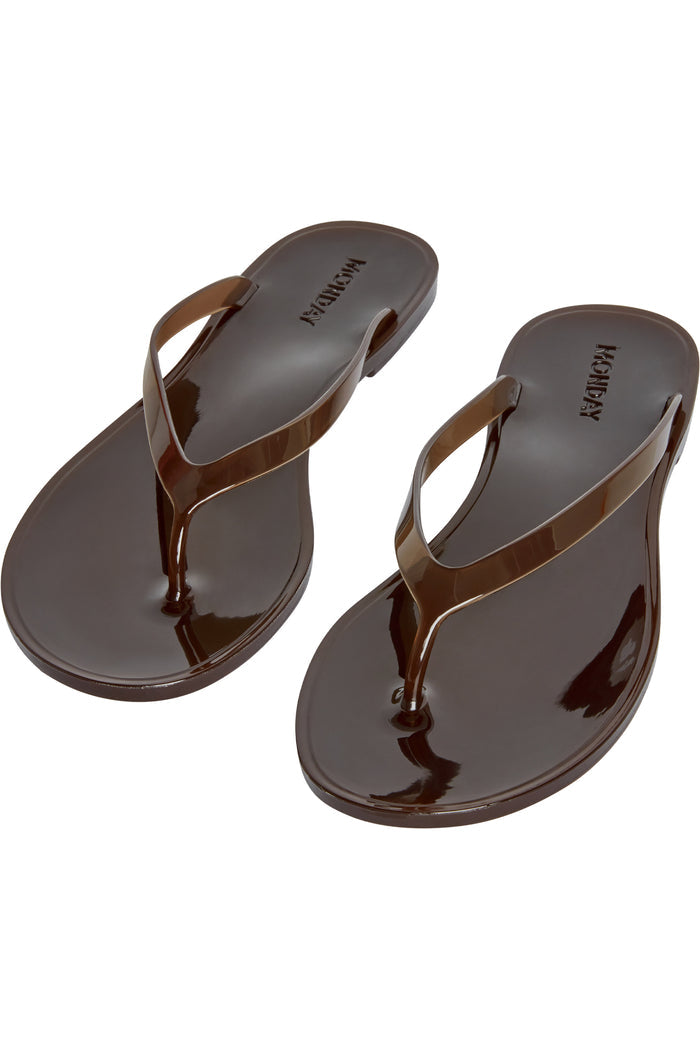 Angled top view of Sardinia Sandal in espresso showing glossy jelly thong straps, slight platform sole, and debossed MONDAY logo on a white background