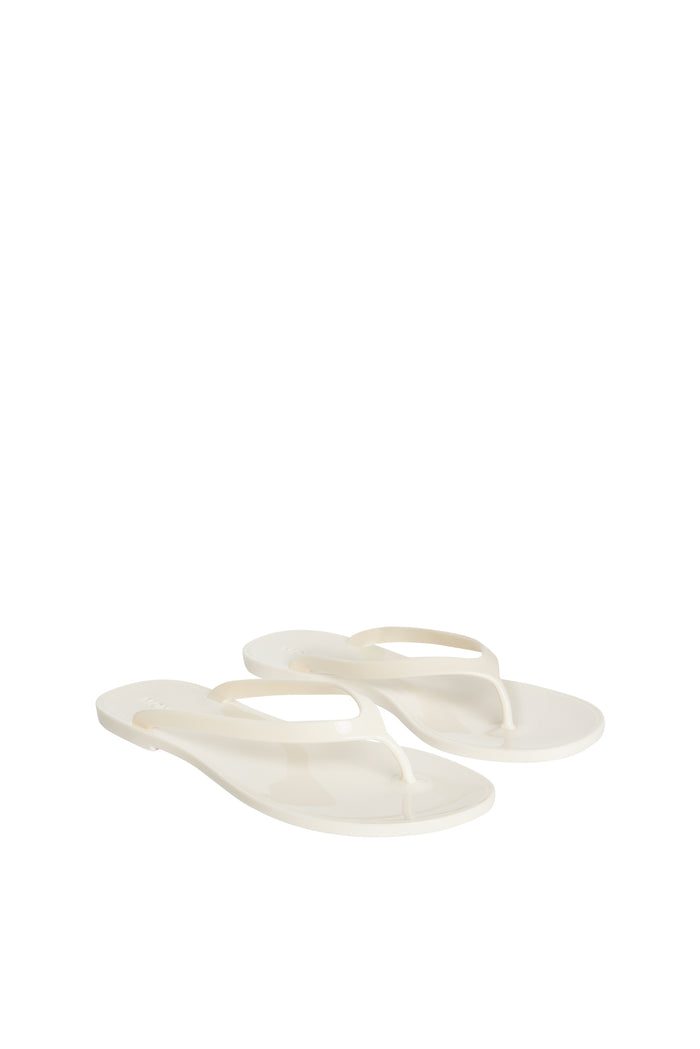 Angled front view of Sardinia Sandal in ivory showcasing glossy jelly flip-flop thong strap and debossed heel logo on white background