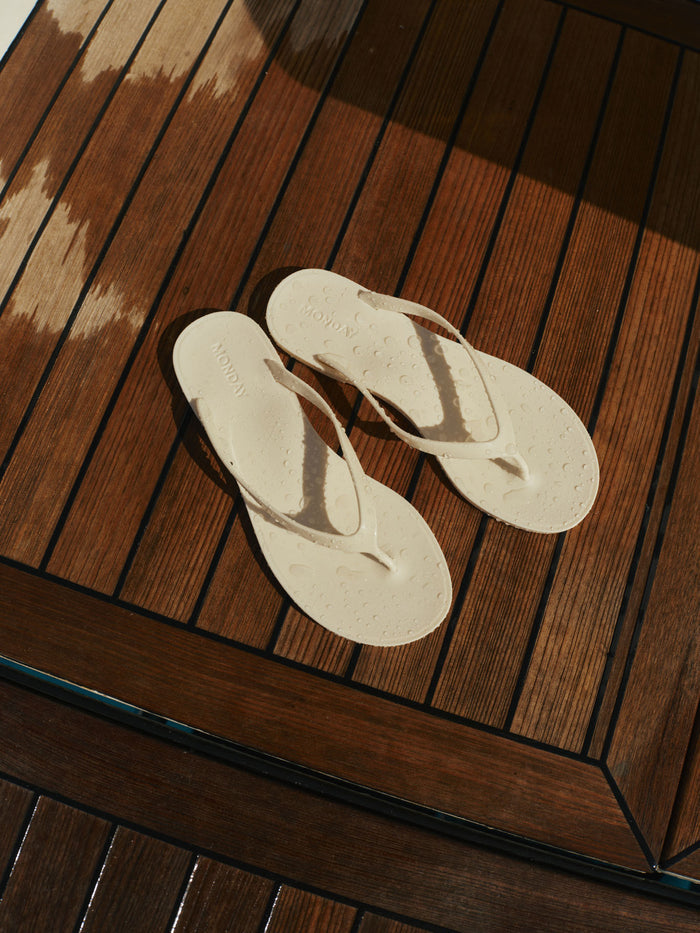 Top-down view of Sardinia Sandal in ivory showing glossy jelly straps and debossed MONDAY logo on the footbed on a wooden deck