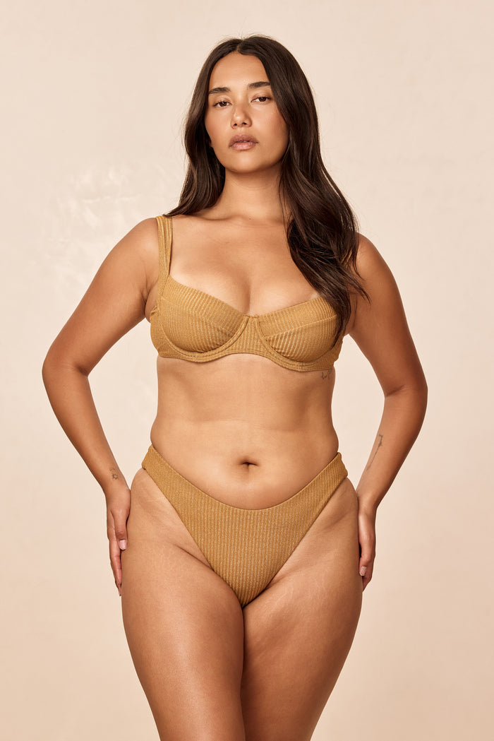 Front of Seychelles bottom in Antique Gold Lurex Rib showing modest coverage, ribbed shimmer on model on beige background