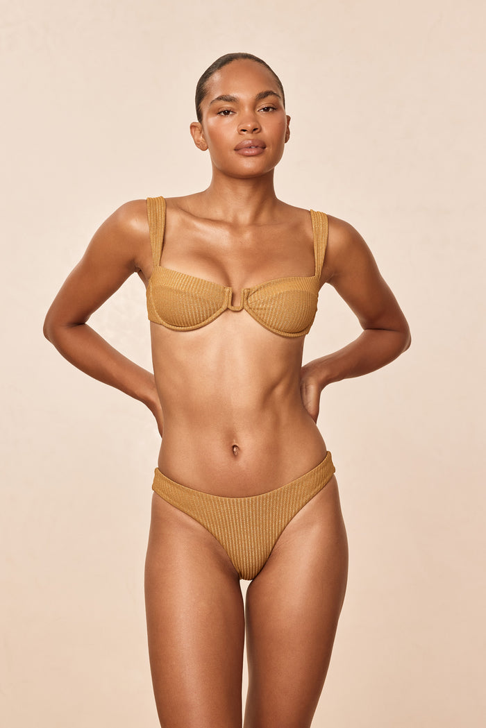 Front view of Seychelles bottom in antique gold lurex rib showing modest coverage on model against beige background