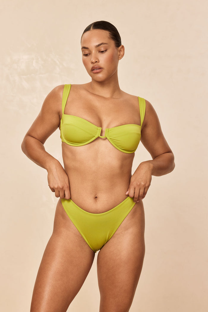 Front view of Seychelles Bottom in Apple on model showing high-cut V-front bikini bottom with smooth fabric, beige background
