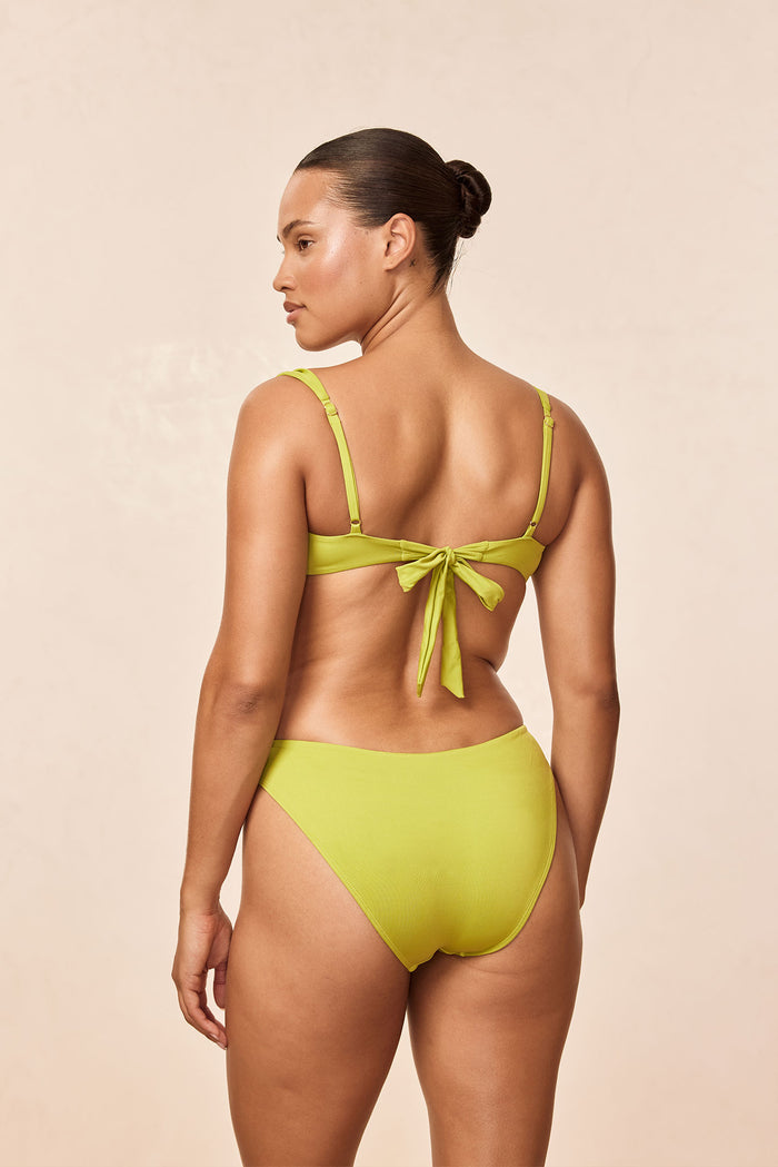 Back view of Seychelles bottom in Apple on model showcasing mid-rise fit and moderate coverage with neutral beige background
