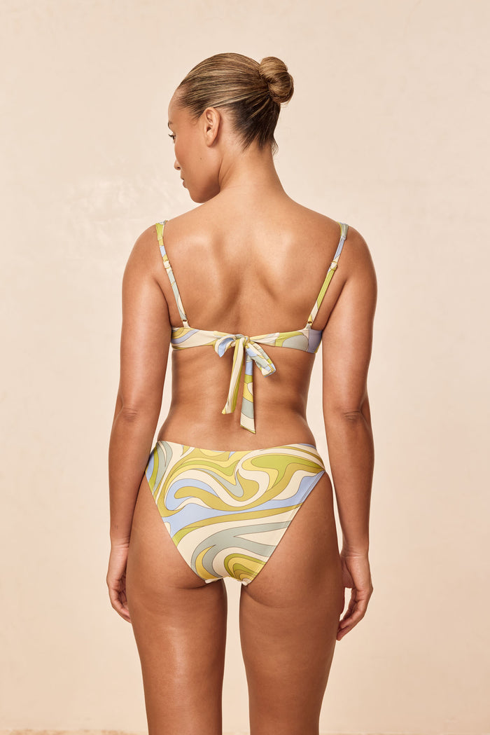 Back view of Seychelles bottom in Costa Rei Apple print on model showcasing moderate rear coverage and swirled pastel pattern on beige background