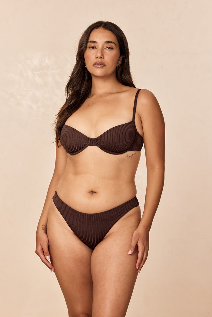 Front view of Seychelles Bottom in Espresso Wide Rib on model showing modest coverage, ribbed texture, and mid-rise fit against a beige studio background