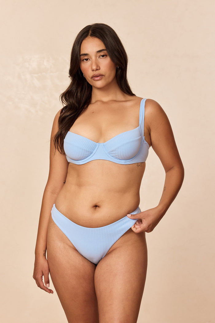 Front view of Seychelles Bottom in Sky Rib on model showing ribbed fabric and high-cut mid-rise fit against beige background