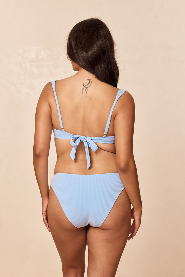 Back view of Seychelles bottom in Sky Rib showing ribbed fabric and moderate rear coverage on model against beige background