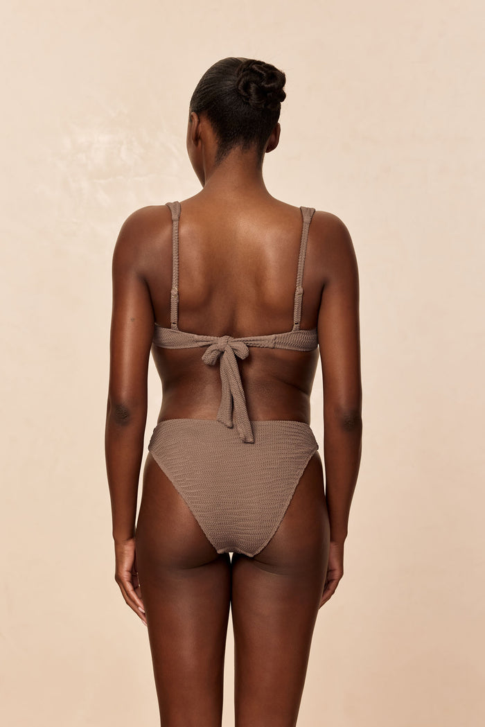 Back view of Seychelles Bottom in Stone Crinkle showing textured fabric and high-rise cheek coverage on beige background