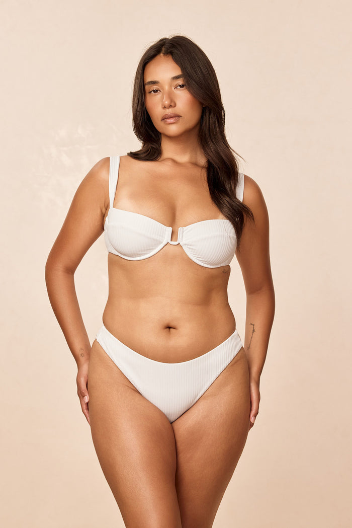 Front view of Seychelles Bottom - White Rib on model, mid-rise moderate coverage with ribbed texture, beige background