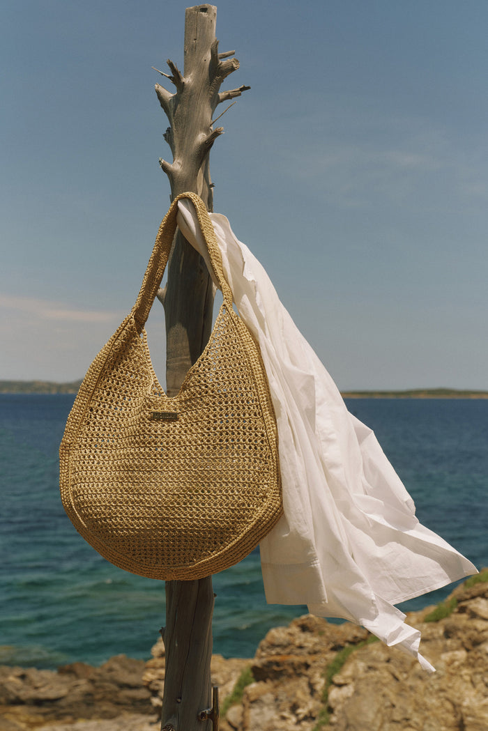 Front view of Shell Beach Bag in Natural showcasing open woven texture, wide shoulder strap, and matching mini pouch by the sea