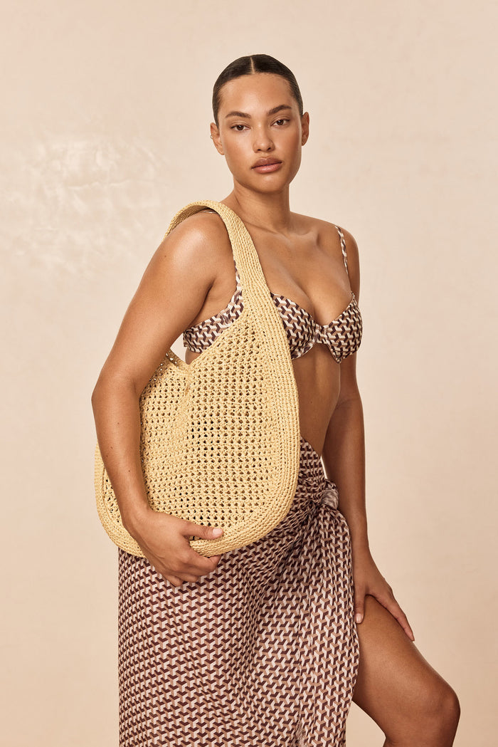 Three-quarter view of Shell Beach Bag in natural showing woven texture and wide shoulder strap against beige background