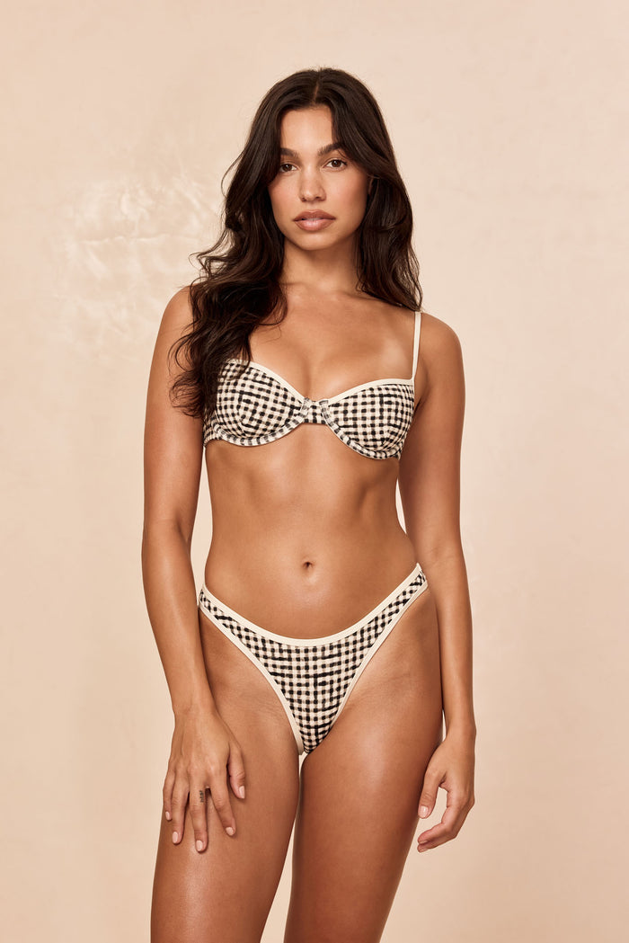 Front view of Somerset Bottom in black gingham on model showcasing high-cut mid-rise cheeky coverage with contrast cream binding against a beige background