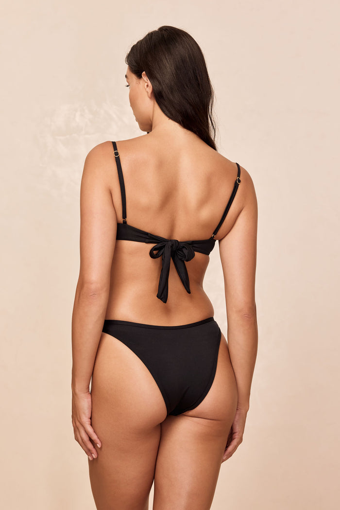 Back view of Somerset Bottom in black showcasing cheeky high-cut leg and binding detail on neutral beige background