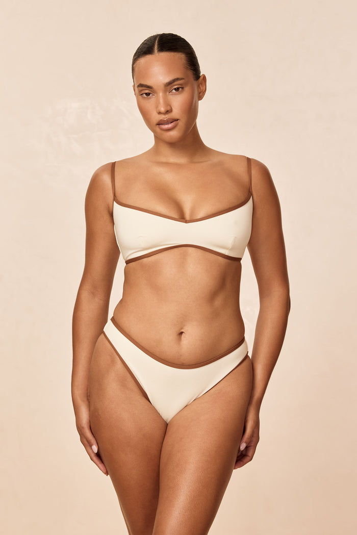 Front view of Somerset Bottom bikini in ivory with caramel trim on model, mid rise high cut on beige background
