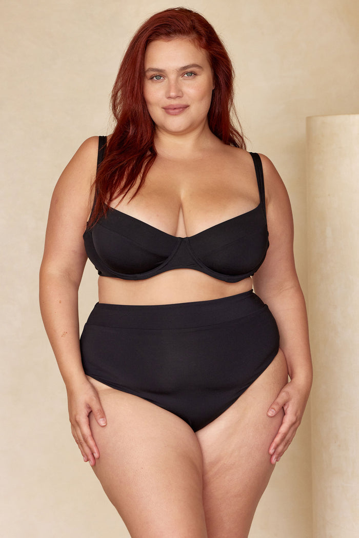 Front view of Sorrento Bottom in black showcasing high-waisted fit and moderate coverage on a plus-size model against a beige backdrop
