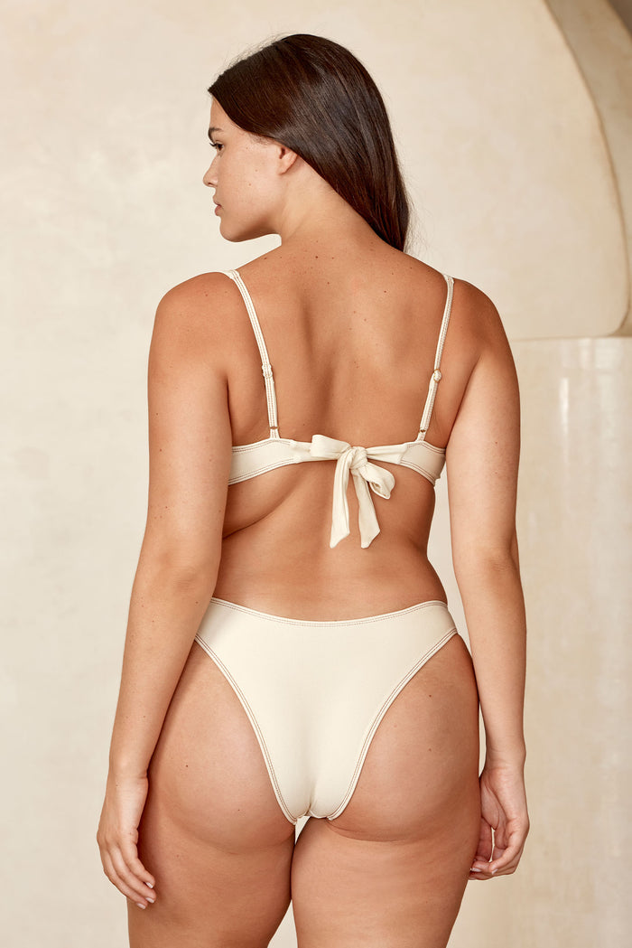 Back view of Sorrento Top in Champagne Denim showing tied back bow and adjustable straps on a beige background