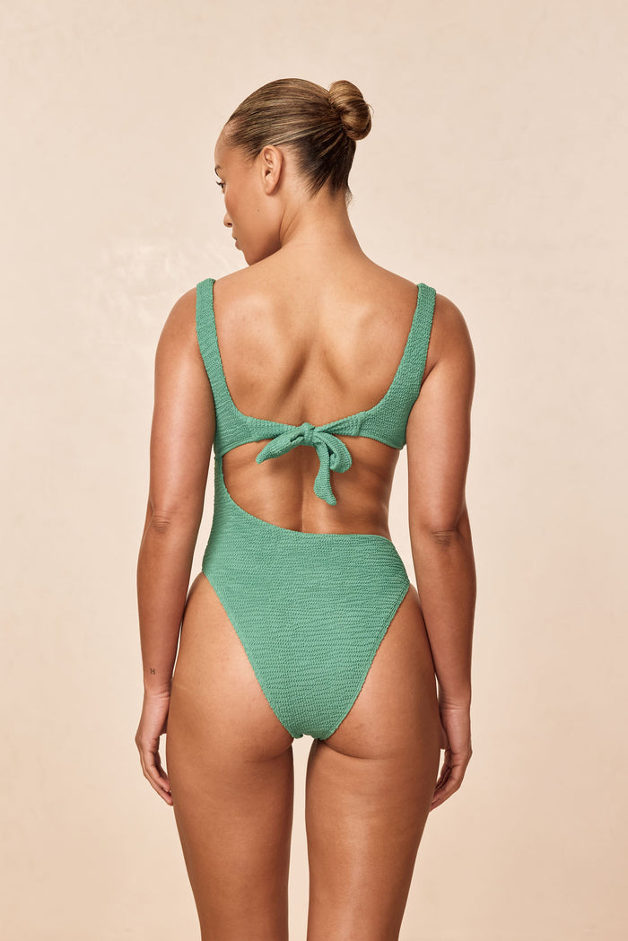 Back view of St. Barth’s One Piece in Pond Crinkle showcasing textured crinkle fabric, tie-back knot and high-cut leg on a neutral beige background