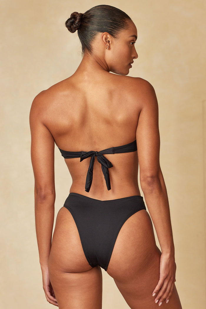 Model shown from back wearing black tie-back bikini top and high-cut bottoms against a neutral background