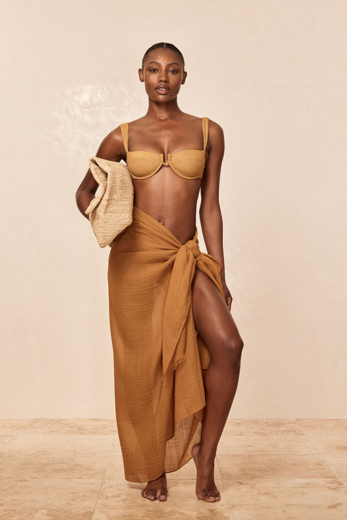 Front view of St. Tropez Sarong in Antique Gold crinkle linen, tied at the hip with a high leg slit on a neutral beige background