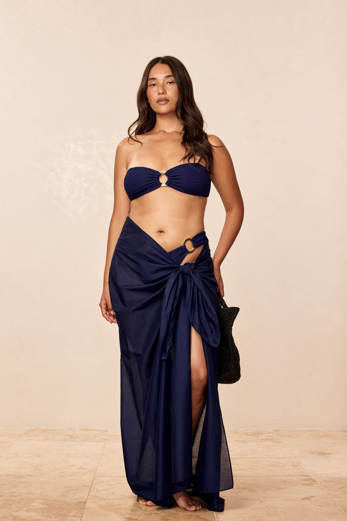 Front view of St Tropez Sarong in Midnight Cotton Voile on model, adjustable semi-sheer wrap with ring detail against beige background