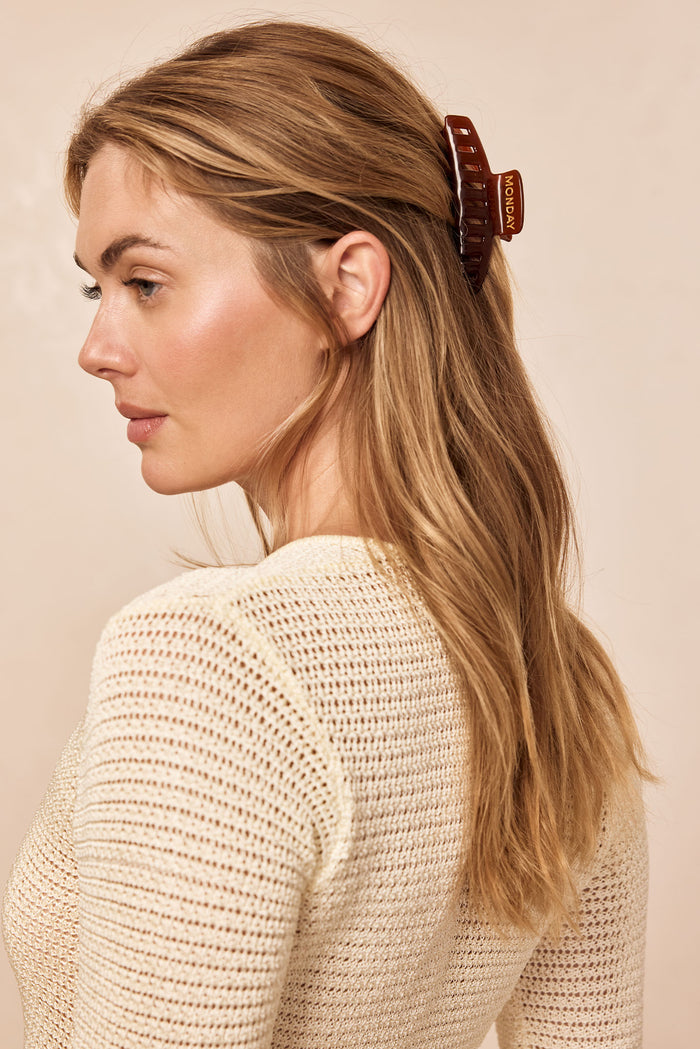 Profile of woman with long blonde hair wearing a brown hair claw labeled MONDAY and a cream knit top.