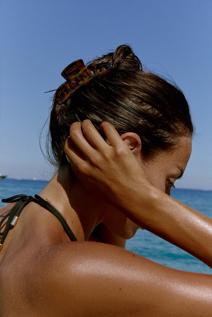 Close-up of tortoiseshell Staniel Cay claw clip showing gold MONDAY logo on hair against ocean background