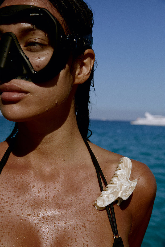 Wet woman wearing a snorkeling mask; pearlescent hair clip reads MONDAY, with sea and distant yacht in background.