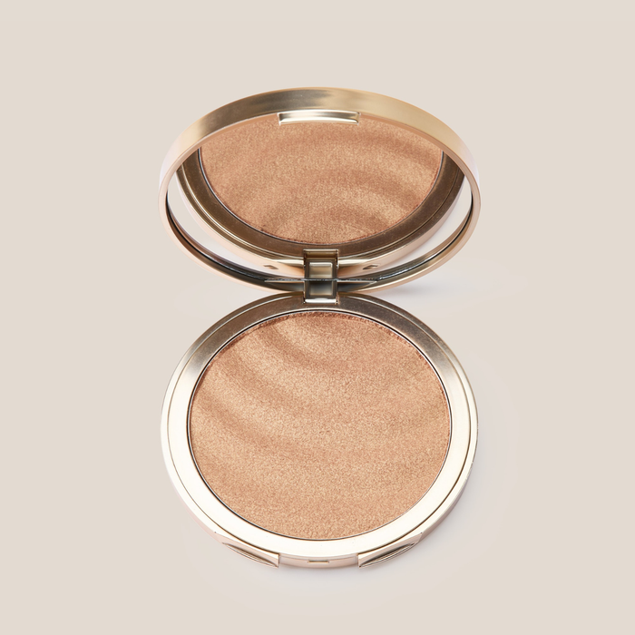 Top-down view of Sun Veil Illuminating Sunscreen SPF 30 compact showing shimmery golden powder and built-in mirror on a beige background