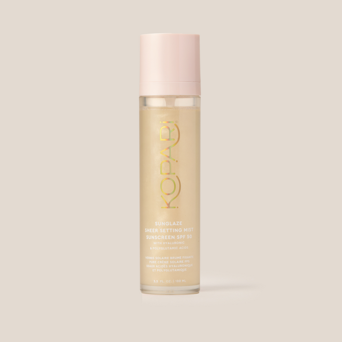 Front view of Sunglaze Sheer Setting Mist SPF 50 bottle with pink cap and translucent gold liquid on pale beige background