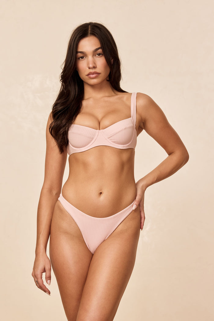 Front view of Tamarama bottom in powder pink rib on model showcasing high-cut leg and ribbed texture against beige background