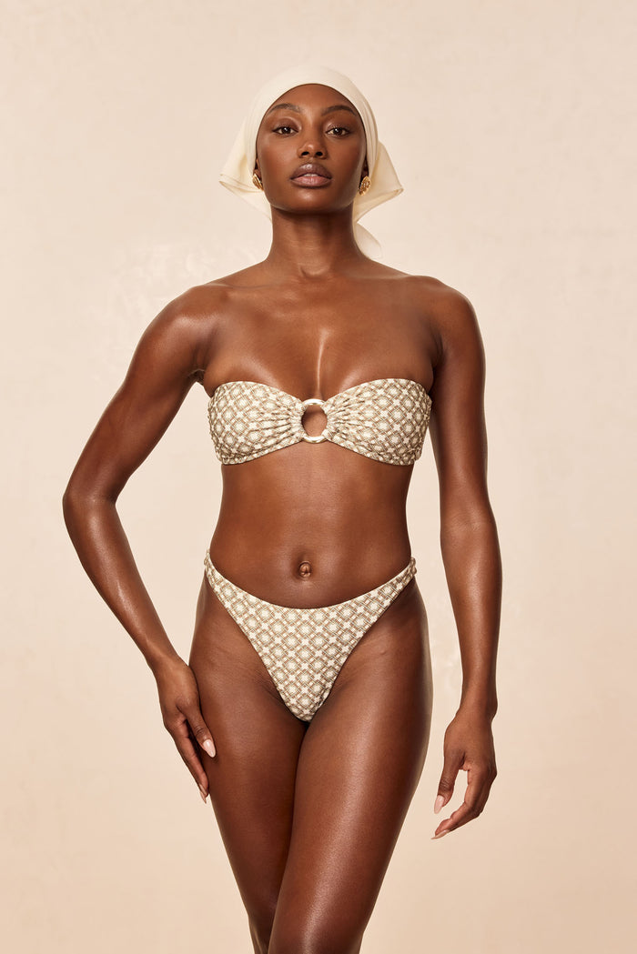 Front view of Tamarama bottom in Tile Geo print on model showing high‑cut V-front and matching bandeau ring, beige background