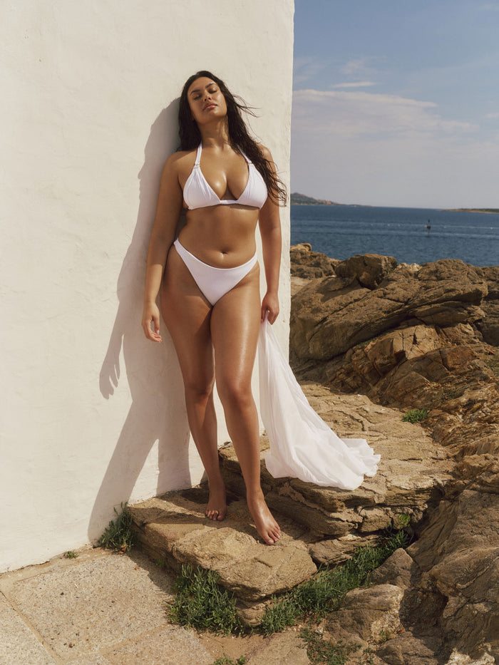 Front view of Tamarama Bottom in Optic White Rib on model showing high leg cut and thin sides against a white wall and rocky shoreline