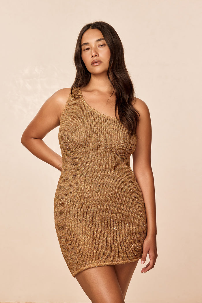 Three-quarter front of Taormina Dress in Antique Gold Sequin Knit showcasing one-shoulder neckline and fitted mini silhouette with neutral beige background