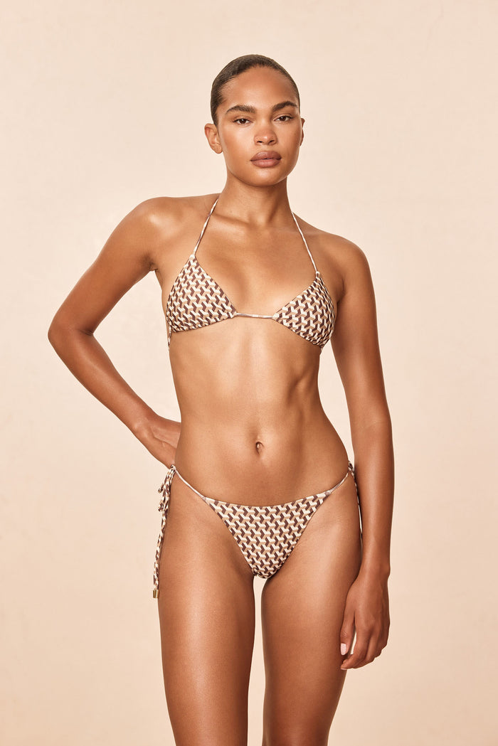 Front view of Taormina Top in Husk Geo showing skimpy triangle cups, thin straps, removable pads and adjustable neck and back ties against a beige background