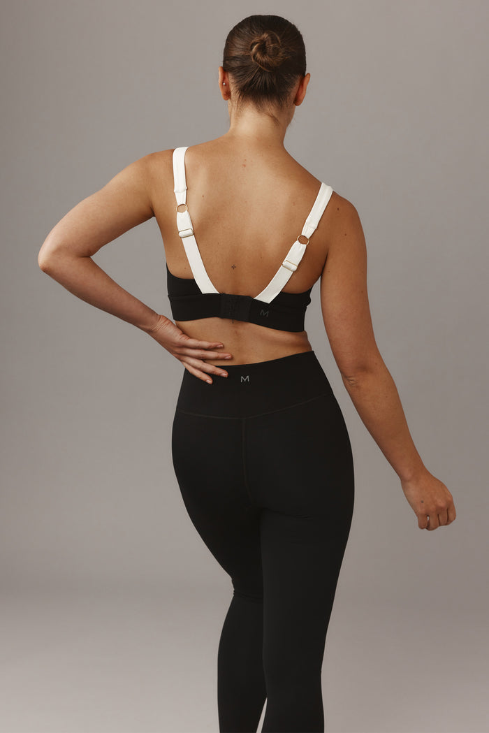 Back view of Tash Bra in black and ivory showcasing adjustable ivory crossover straps and hook-and-eye band with M logo on neutral background