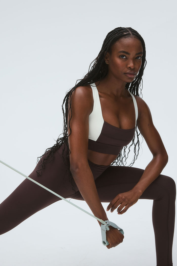 Three-quarter view of The Tash Bra in Espresso/Ivory, showing wide ivory straps and supportive band on a model lunging