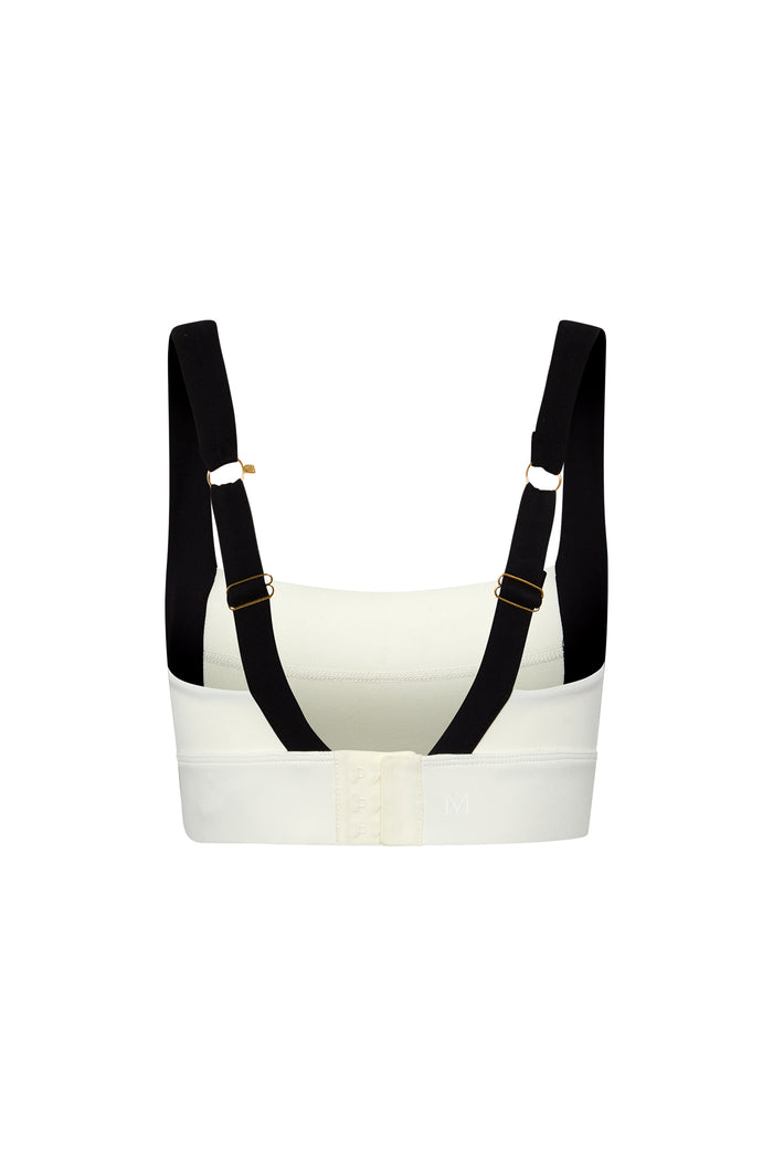 Back view of white sports bra with wide black adjustable straps, gold hardware and three-column hook-and-eye closure; embossed 'M' on band.