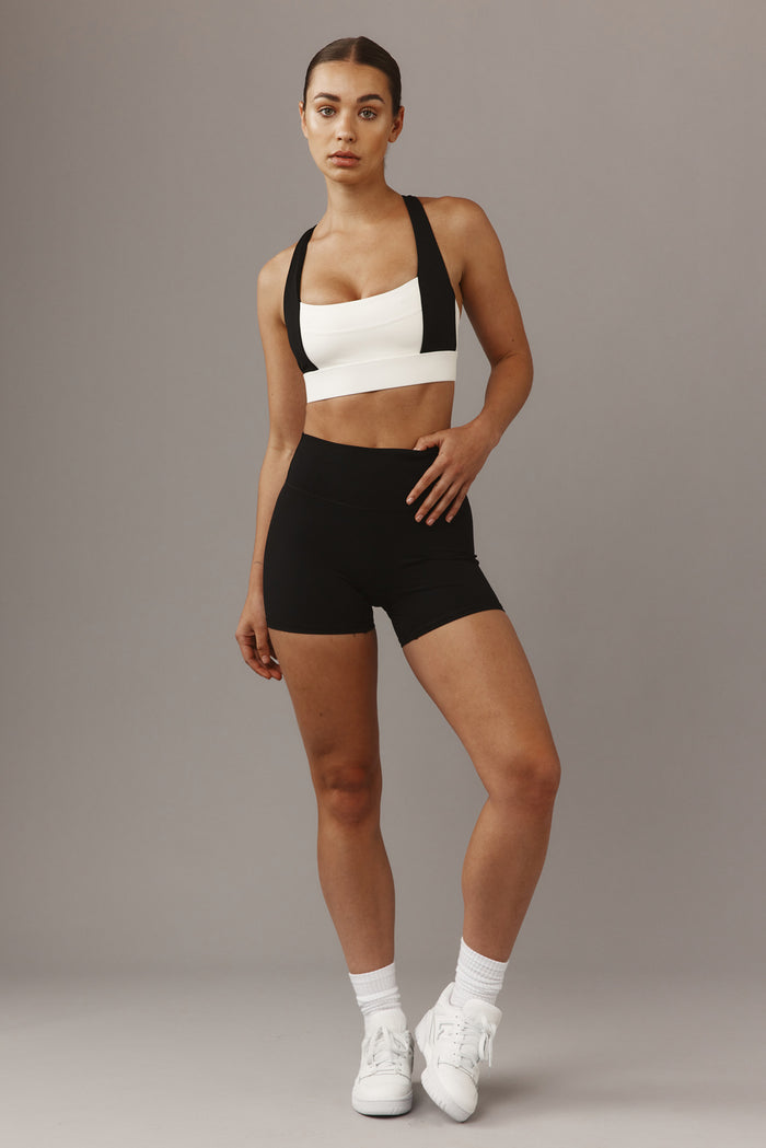 Three-quarter front view of The Tash Bra in ivory/black on model showing wide black straps and supportive underband