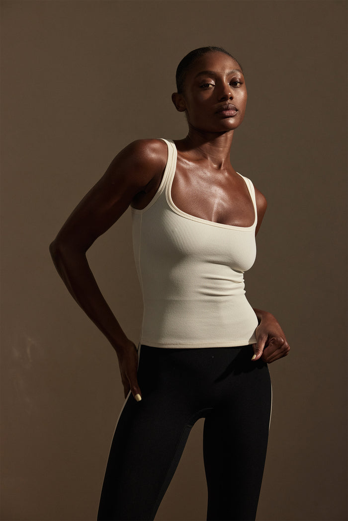 Front three-quarter of Tash Tank Long in Ivory Rib on model showcasing ribbed texture and square neckline on warm studio background